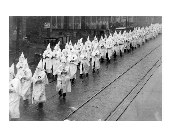 Ku Klux Klan (KKK) wearing iconic masks and white robes parading down King Street to Schroeder Funeral Home for the funeral of Police officer Herbert Dreger. Dreger was shot to death in "Death's Corner" (South Murray Street) on December 2, 1924.