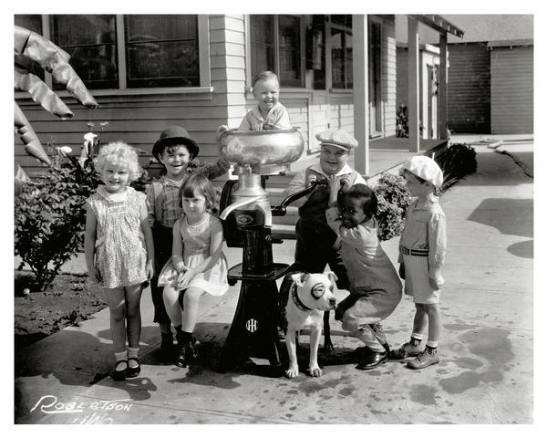 Cast members from the early 20th century film series "Little Rascals" pose in and around an International Harvester cream separator with their dog.