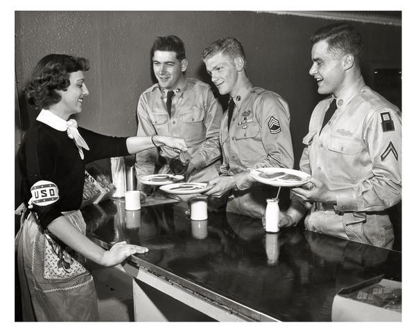 A smiling USO staff worker serves pancakes to hungry soldiers.