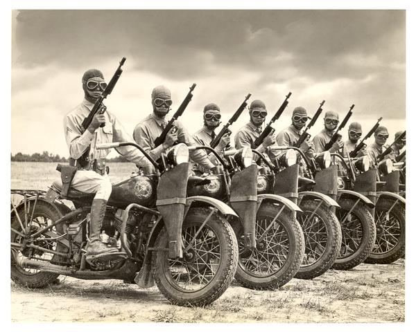 World War II Harley-Davidson Army Models mounted by ever-alert Military Police, wearing uniforms and armed with guns.