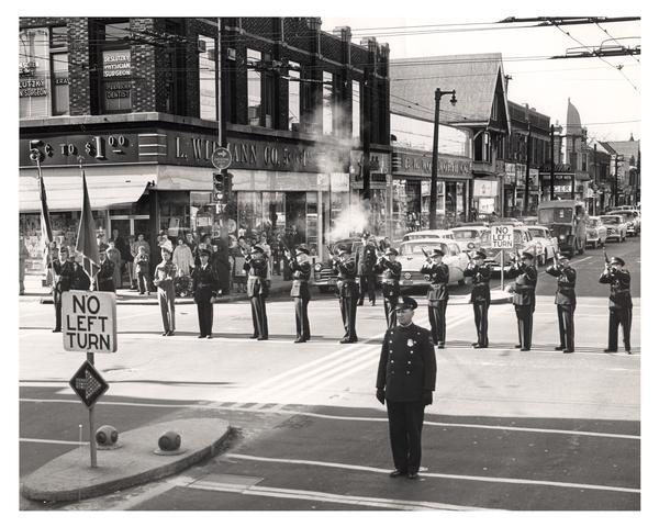Uptown Post #400 Drill Team in formation firing a salute on Armistice Day while passers-by pause to pay their respects.