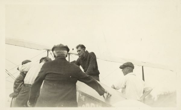 Men gathered around airplane. Clarence Russell? on right side.