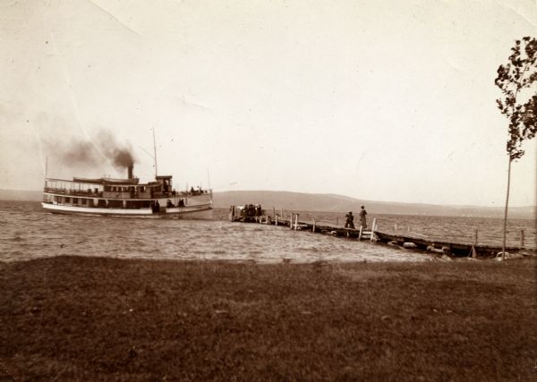 View from shoreline of the steamboat "Plowboy" approaching the Mission Dock at La Pointe. The Plowboy was the first steam ferry to go to Madeline Island. The boat made regular runs between Ashland, Washburn, Bayfield, and La Pointe.