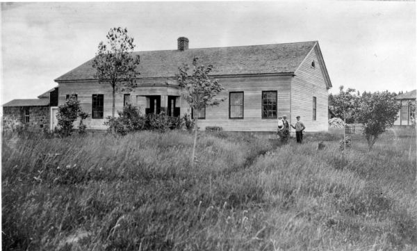 George F. Thomas is holding a child and standing next to Edward F. Hansen in front of Treaty Hall in La Pointe on Madeline Island.