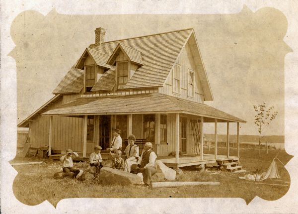 The Woods family sitting in yard outside house on Nebraska Row, La Pointe, Madeline Island. The house was built in 1904. Left to right: Twins Tom & Henry Woods, Mr. George Woods, unidentified son, Mrs. Woods, and Colonel Woods.