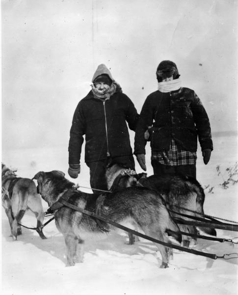Two men standing next to dog team on frozen Lake Superior.