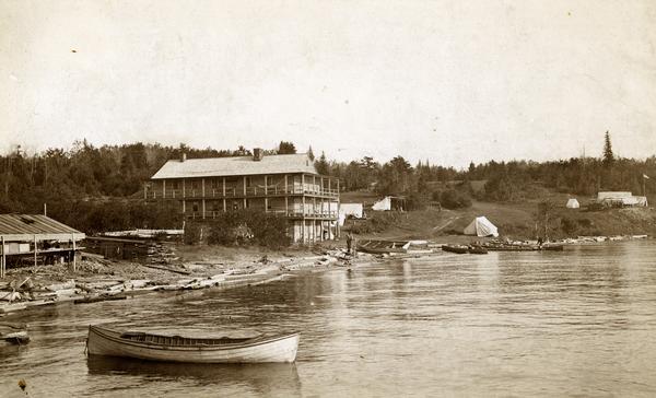 Old Mission Inn and boats on shoreline of Lake Superior on Madeline Island. The Old Mission Inn had numerous modifications over the years.  It was razed in 1965.
