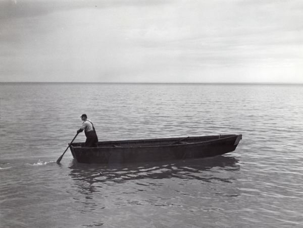 Lone man boating or fishing alone on Lake Superior. He is standing at the rear of the boat holding an oar.
