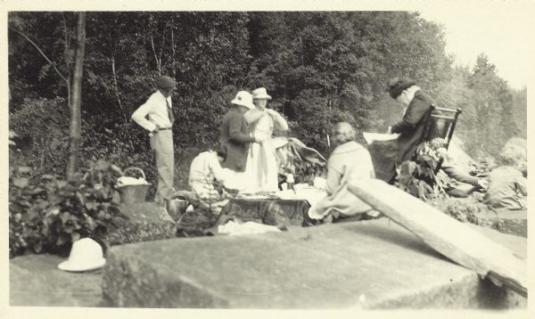 Group of people at a picnic on the shoreline at Bass Island. Names written on back of print: Mrs. Abernathy, chair; Mrs. Hull; Mrs. Baker.