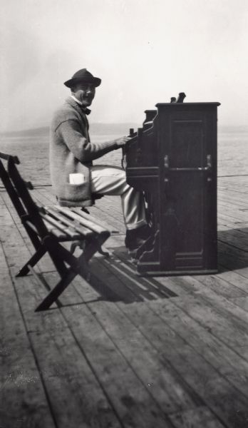Leo Capser, founder of the Madeline Island Historical Museum, sitting on a bench playing piano on the Old Mission Dock at Madeline Island.