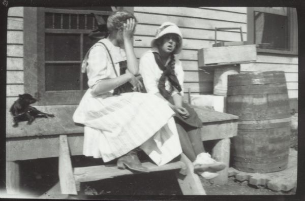 Two girls and a girl sit on the wooden stoop near a door. Grant's Point farm, Madeline Island.