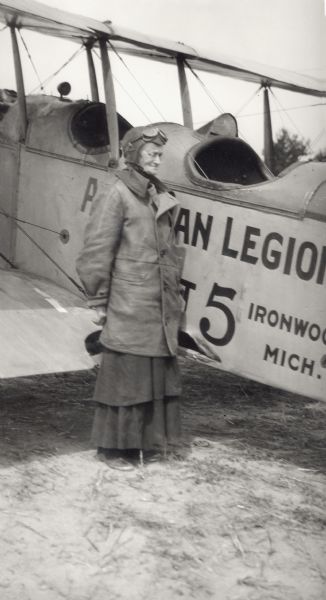 Postmistress Mrs. Lathrop poses next to Harold Russell's airplane. This plane was the first to land on Madeline Island.