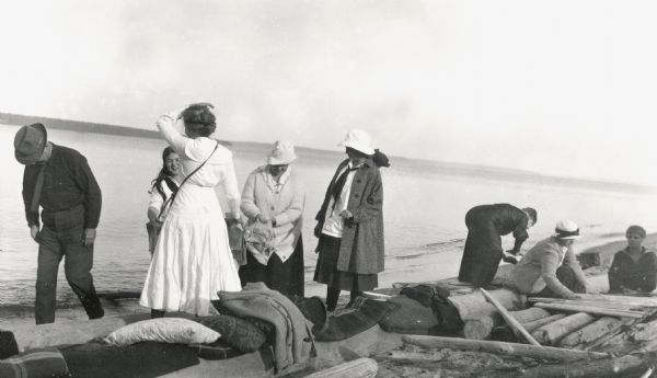 Group setting up for a picnic at the shoreline on Bear Island of the Apostle Islands. Image includes A.G. Hull, Elizabeth Nisbet (Mrs. S.C. Marty Sr.), Elizabeth Baker, Mrs. Baker, Louise Baker, Mrs Hull, and Florence Baker.
