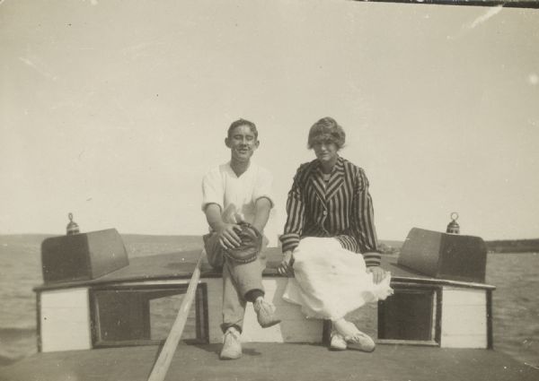 Two people sitting on a boat. Identified on back as Betty Bishop and Wallace? Wallace is wearing a baseball mitt on his left hand.