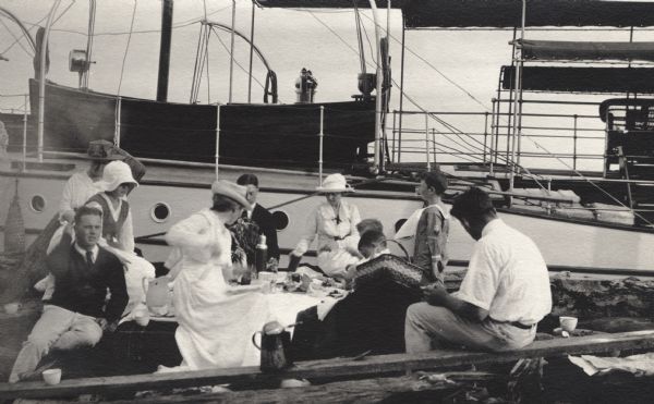 Group having a picnic on the shore of an Apostle Island. There is a large sailboat behind the group.