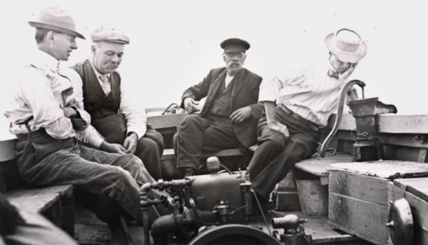 Four men aboard the "Lucy" on Lake Superior. Andrew Siem is the boat owner and is operating the tiller. Man with moustache identified as N.J. Ross.