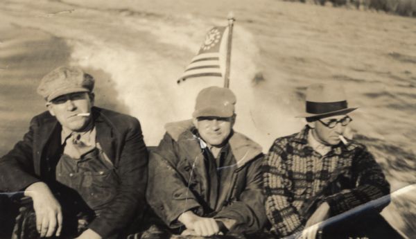 Three men power boating on Lake Superior. Two of the men are smoking cigarettes.