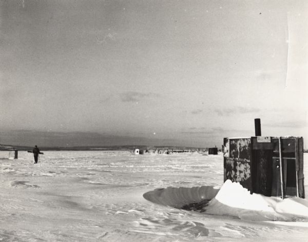 George Harris and other ice fishing shanties on Chequamegon Bay. One man is on skis moving across the snow and ice.