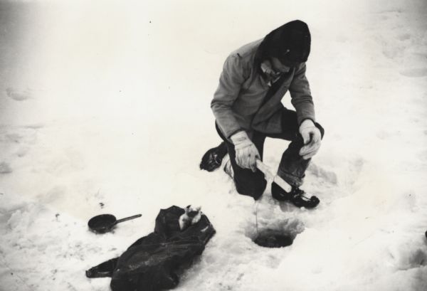 Man ice fishing on Chequamegon Bay through a hole with a fishing jig, fish and fry pan.