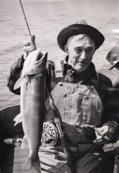 A fisherman sitting in a boat is holding a cigar and posing with lake trout.