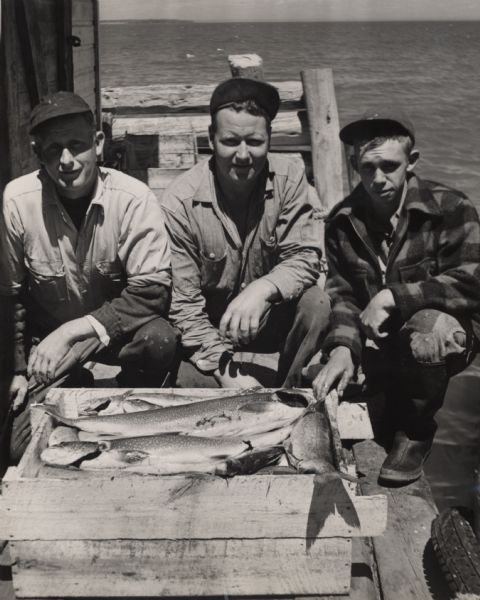 Catch of lake trout displayed by three fisherman on the pier at Little Sand Bay. From left to right are Martin Johnson, Hermy Johnson, and Myron Lohman.