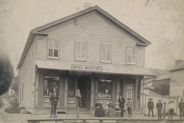 Exterior view of Charles Pfeifer's Drugstore, founded in 1858. From left to right are Charles Pfeifer, Fred Pfeifer, Mrs. Adam Heeb, Fulda Pfeifer, Mrs. Charles Pfeifer, Wera Pfeifer, Adam Heeb, and Eddie Pfeifer.