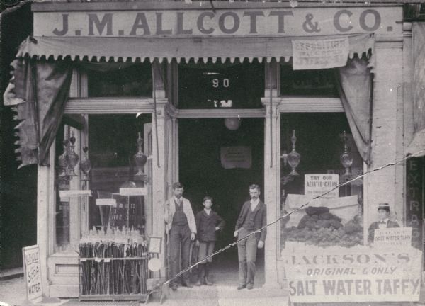 Exterior of the drugstore of Joseph Mabbett Alcott at 90 Wisconsin Street. Pictured are Charles Alcott (left), his son, and store helpers.