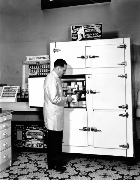 Gilbert Holscher, store owner, investigates the stocks of biologicals in one of the store's 2 refrigerators. The card on top of the refrigerator was used on area bus advertisements.