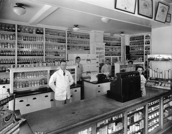 Staff members of the Affleck Pharmacy stand behind the prescription pick-up counter. The proprietor, A.J. Affleck, is in the foreground.