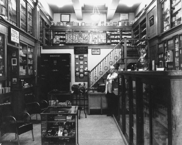 Interior of pharmacy with the prescription case.  Standing by the stairs is D.F. Jones, store proprietor.