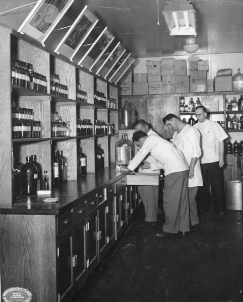 A group of pharmacists consult each other at one of the counters in the laboratory. Pictured are, from left to right: William Hays, Steve Kostyk, Urban Korcsmar, and Andy Tomsik.