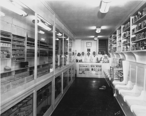 The entire staff of Tozer Pharmacy poses in the rear of the store. The laboratory is on the left, with benches for customers who are waiting on the right. This arrangement allowed customers to watch their medications being prepared.