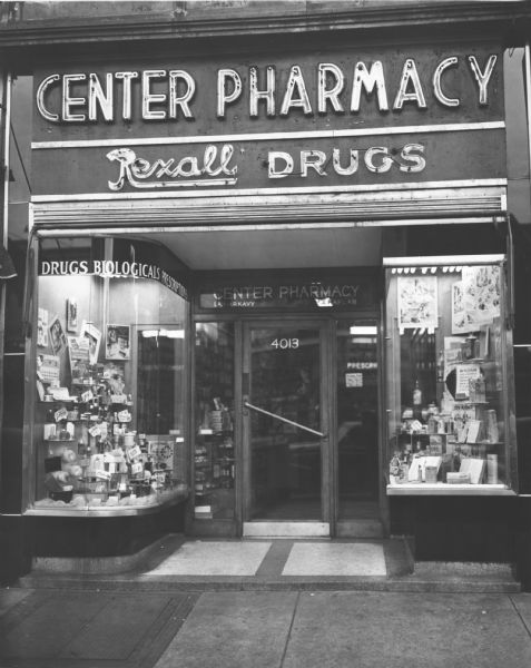 Exterior view of the display cases and neon sign frontage of the Center Pharmacy, a Rexall affiliate.