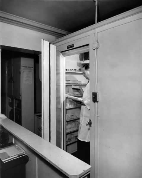 A pharmacist checks the stocks of biologicals in a large, modern "walk-in" refrigerator.