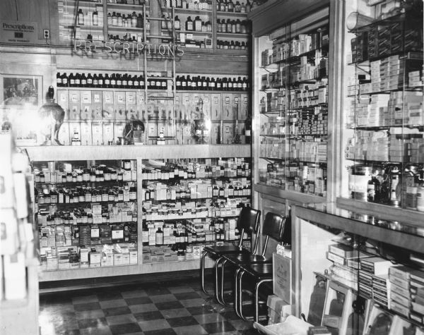 View of the prescription counter and waiting area of the Center Pharmacy. The ladder provided access to shelves of medications held above the counter.
