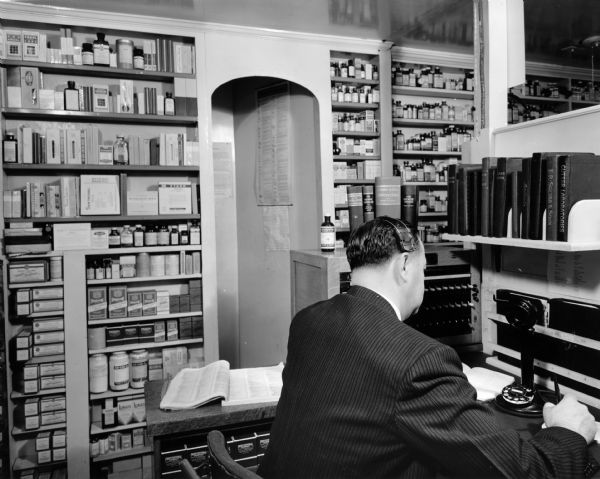 Druggist J.F. Robinson staffs the pharmacy's "Information Desk,"  ready to take a prescription from a doctor over the telephone.  The pharmacy championed this as a modern time-saving measure for customers.