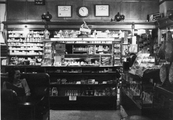 One of the customer service counters at Meyer's Pharmacy. The counter is stocked with a variety of personal grooming and cosmetic items, like hair oil. A sign behind the counter indicates that the pharmacy sold money orders as well as provided the services of a notary public.