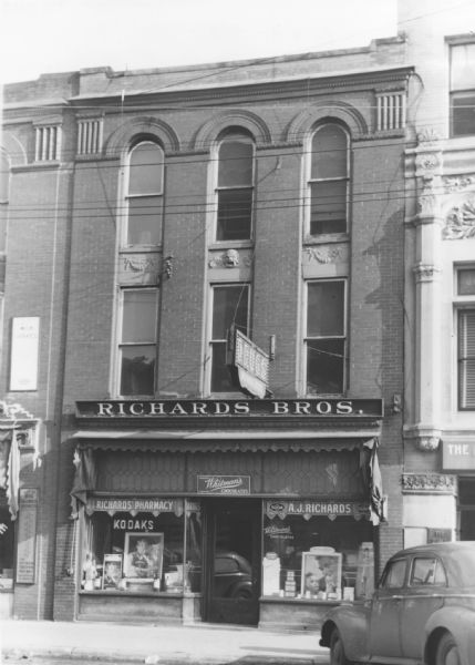 Exterior view of Richards Brothers Pharmacy. Featured prominently on the exterior are signs for both Kodak Film and Whitman's Chocolates.