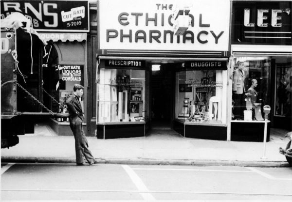 A young man waits beside his delivery truck in front of the storefront for the Ethical Pharmacy.