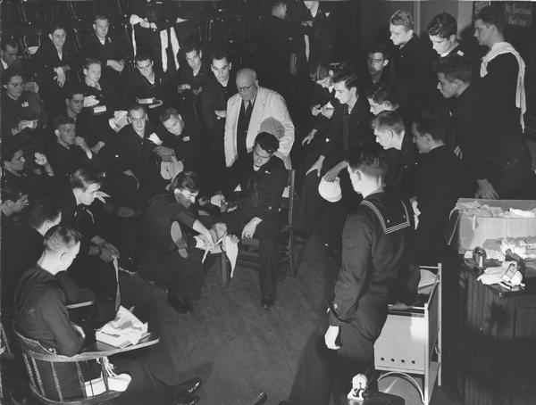 One member of the U.S. Coast Guard Hospital Corps class demonstrates the method of treating a leg injury while fellow classmen look on and make notes. The training of these Pharmacists' Mates helped to off-set the shortage of physicians and trained pharmacists aboard small vessels of the Coast Guard.