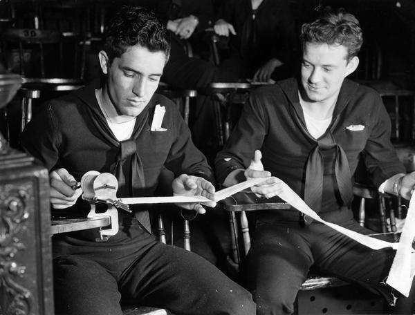 Two members of the U.S. Coast Guard Hospital Corps School roll bandages with the help of a crank-operated machine. Part of their training involved the preparation and application of surgical dressings and general first aid.