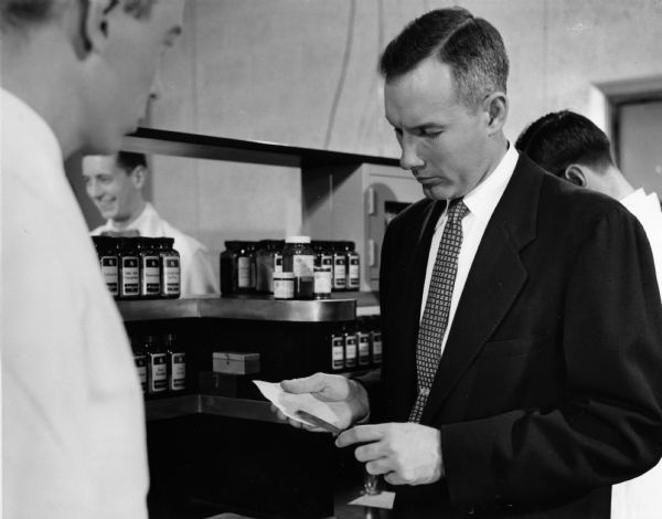 A professor checks a prescription prepared by a pharmacy student in this lab scene from "Time for Tomorrow". Women, as well as men, can find a rewarding career in hospital pharmacy, as depicted here in a shot from "Time for Tomorrow", a film produced by the American Association of Colleges of Pharmacy and the American Foundation for Pharmaceutical Education. The film shows student life in the lab, the classroom, and on campus.