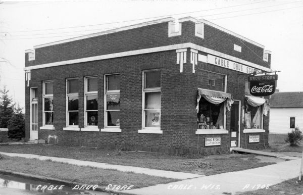 View of exterior of the Cable Drug Store. The signs on the exterior advertise that they have a soda fountain with Russell's Ice Cream and Coca-Cola.