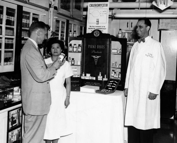 Noted pioneer of Hospital Pharmacy, Donald Francke,
examines an item from a display of pharmaceuticals from the Parke Davis Company, while the chief pharmacist and his assistant look on.