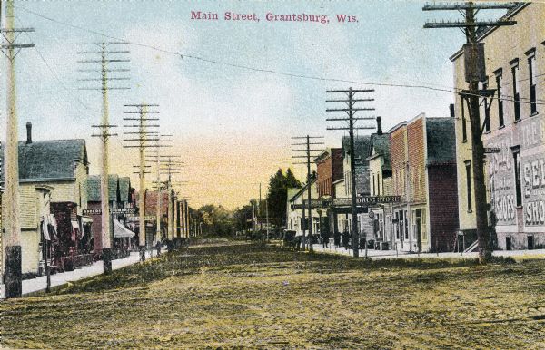 View of various businesses on unpaved Main Street, including a drug store on the right side. Caption reads: "Main Street, Grantsburg, Wis."
