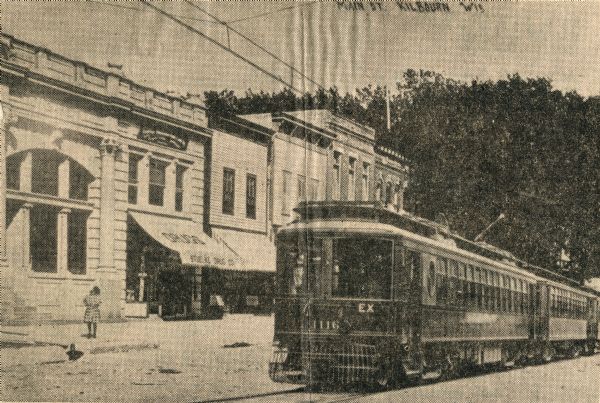 A streetcar apparently zips along down the center of Broadway, the town's main thoroughfare. The structure with the awning (to the right of the old bank building) was occupied by Stuelke's Drug Store when this photograph was taken. This car (1116) was part of The Milwaukee Electric Railway & Light Company's fleet of interurbans built by St. Louis Car Company just before the turn of the century.  While The Milwaukee Electric Railway and Light Company spread from Kenosha to Sheboygan and Burlington to Watertown, they never reached Wisconsin Dells.  This is one of a vast series of fake trolley photographs published in the first decade of the 1900's.