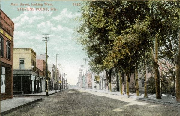 View of a Main Street. A drugstore can be seen prominently on the left. Trees line the sidewalk on the right. Caption reads: "Main Street, looking West, Stevens Point, Wis."