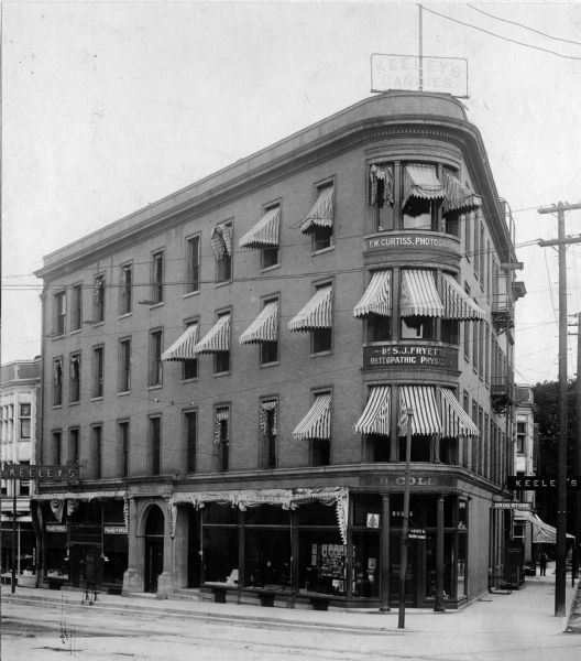 View of the Wisconsin Building at 102 State Street and Carroll Street, built around 1901. The majority of the building was then occupied by Collyer's Drugstore. Other establishments were Keeley's Palace of Sweets, Dr. S.J. Fryette, Osteopathic Physician, and F.W. Curtiss, photographer. This was later the site of the Commercial State Bank.