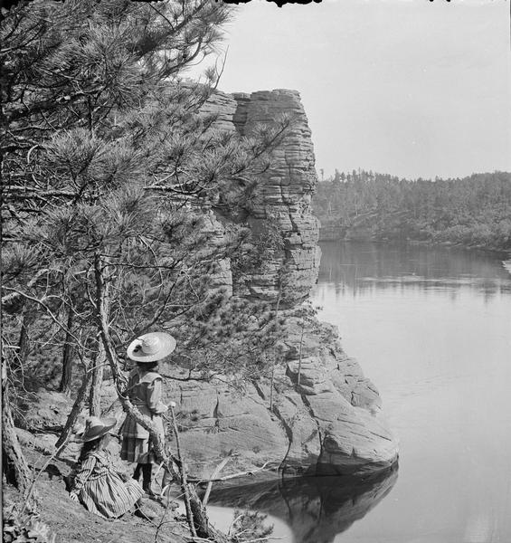 High Rock; upstream side. Two girls are looking out at the river. The girl at the left is sitting, and the girl next to her on the right is standing.