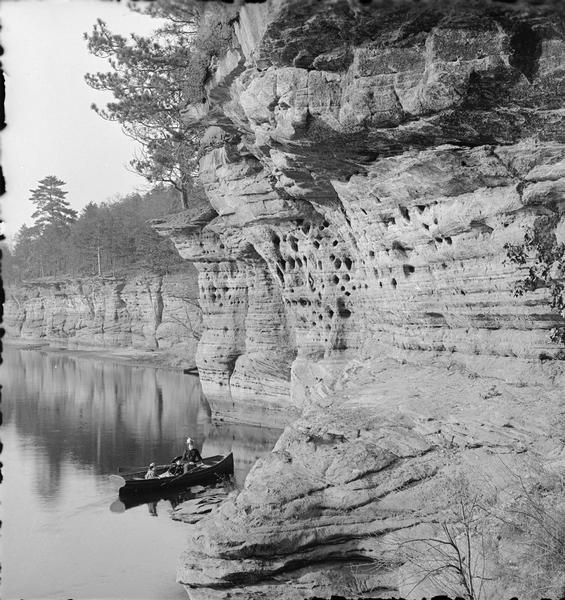 South face of Swallows Nest in the Wisconsin Dells. Ruth, Miriam and Evaline Bennett are in a rowboat near the shoreline.